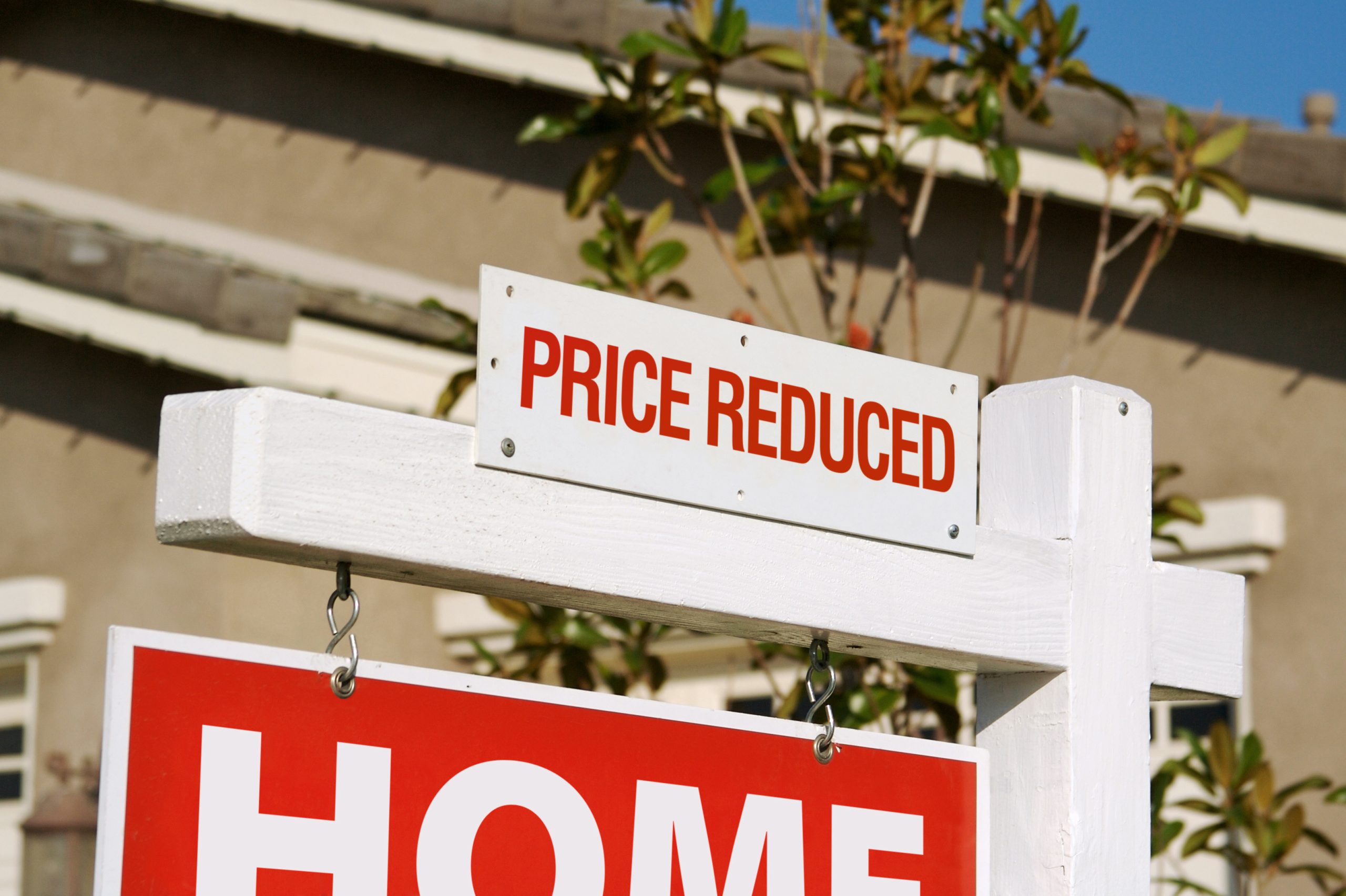 A sign showing an downward arrow in front of a house. Concept of declining markets in real estate