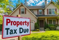 A family home with a "Property Tax Due" sign on the front lawn, emphasizing what you need to know about your Texas property tax bill